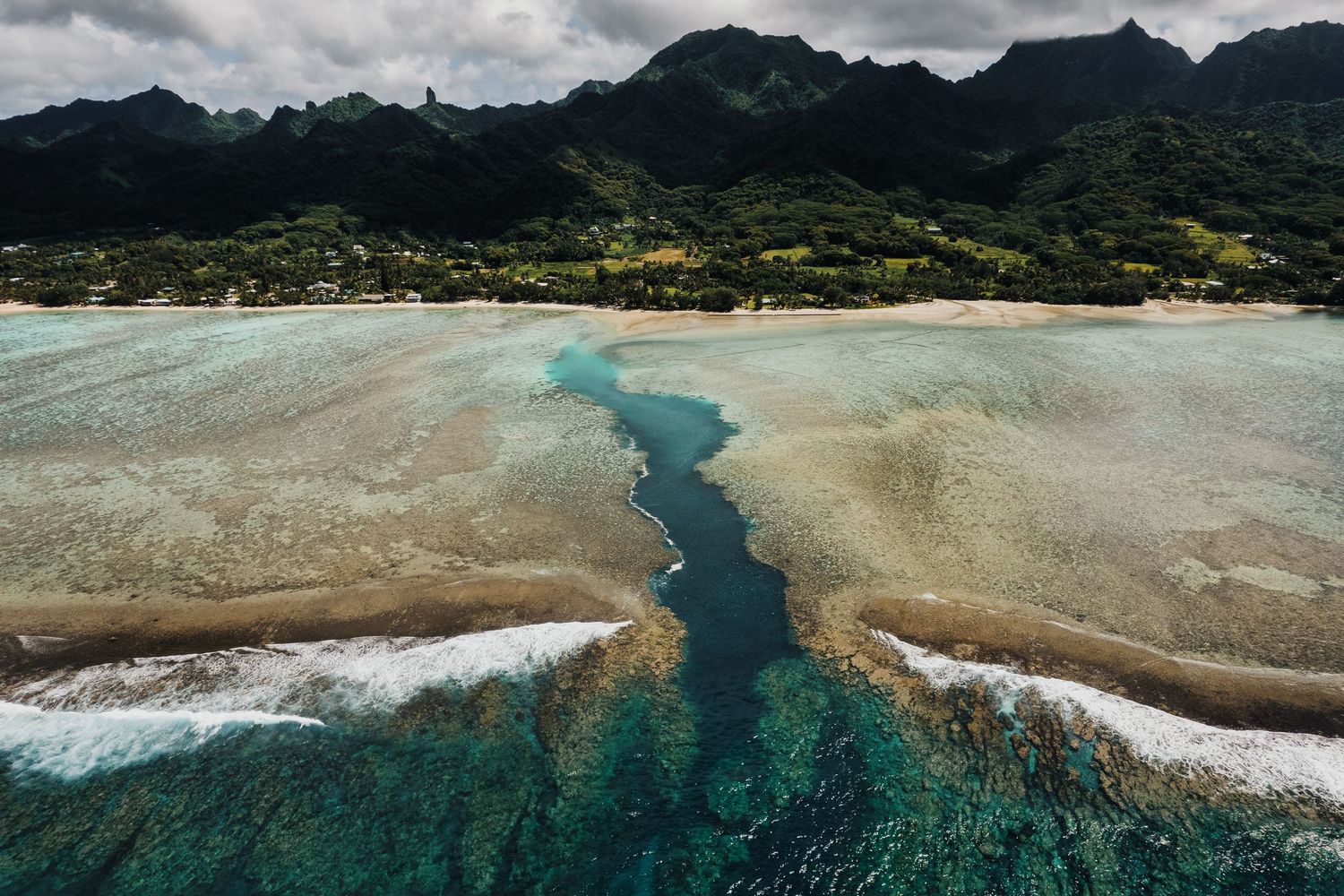 Aerial view of a coral reef channel cutting through turquoise waters near a tropical coastline.