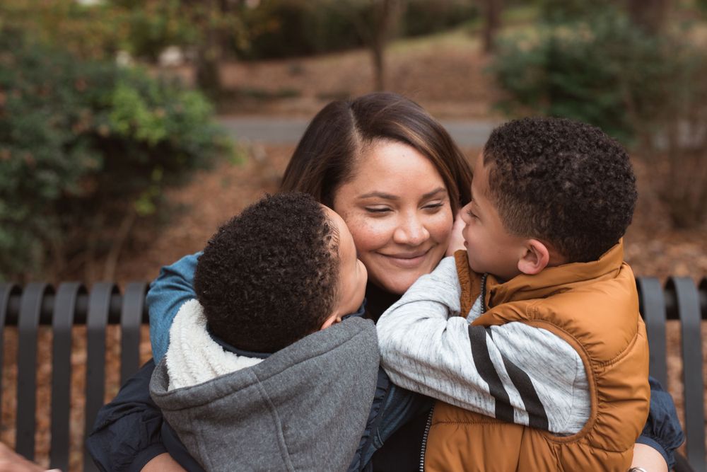 black children kissing mother while sitting on park bench
