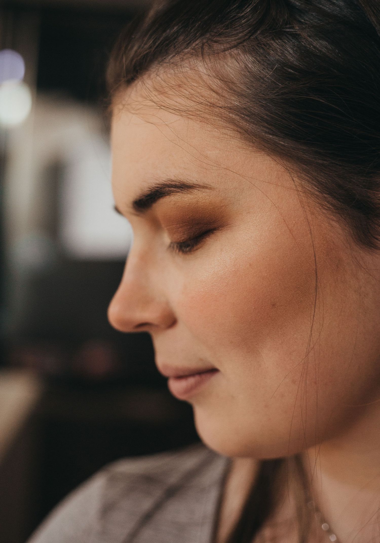 Side profile portrait showing natural makeup and glowing skin in warm lighting.