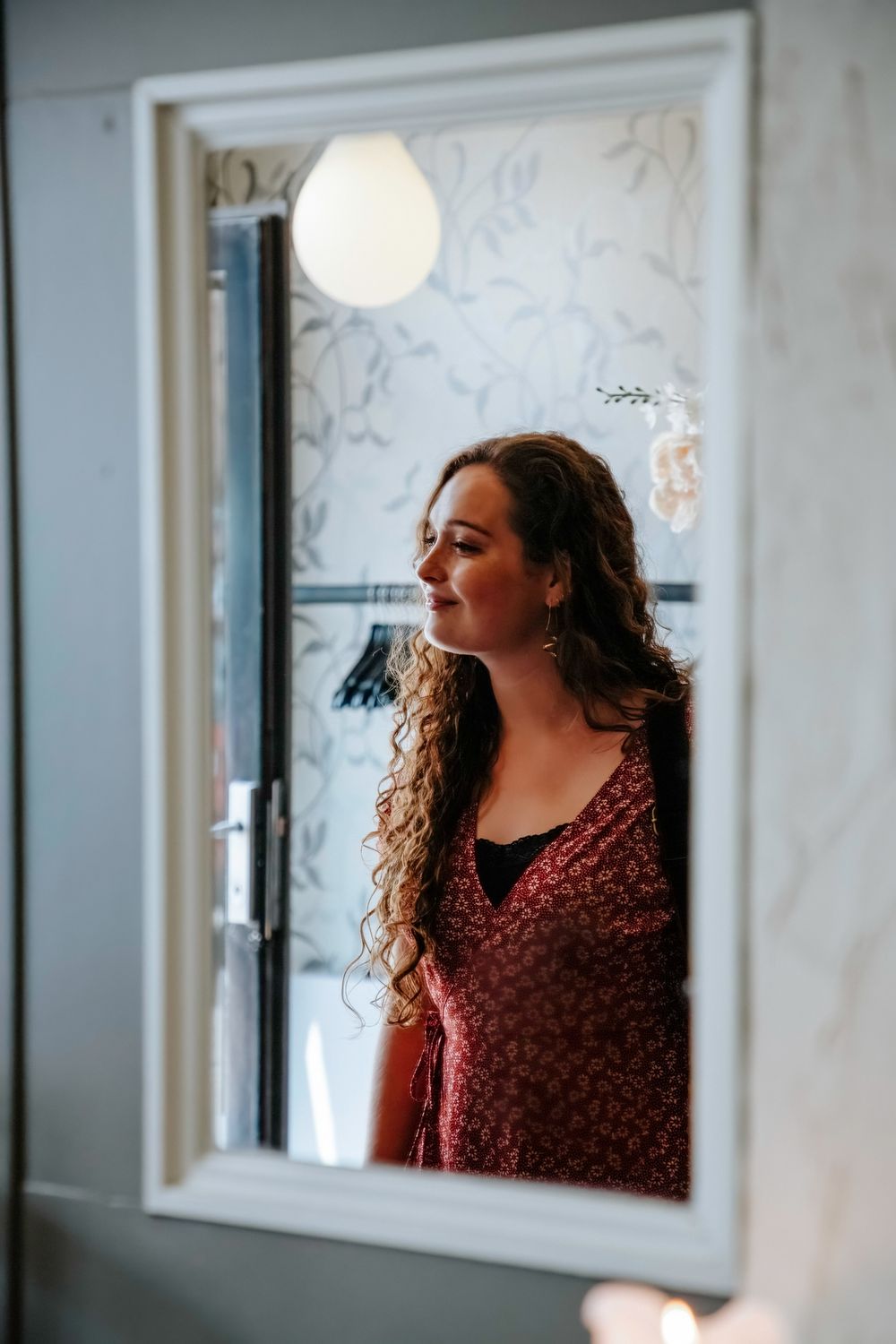 Mirror reflection shows person in burgundy dress standing in doorway.