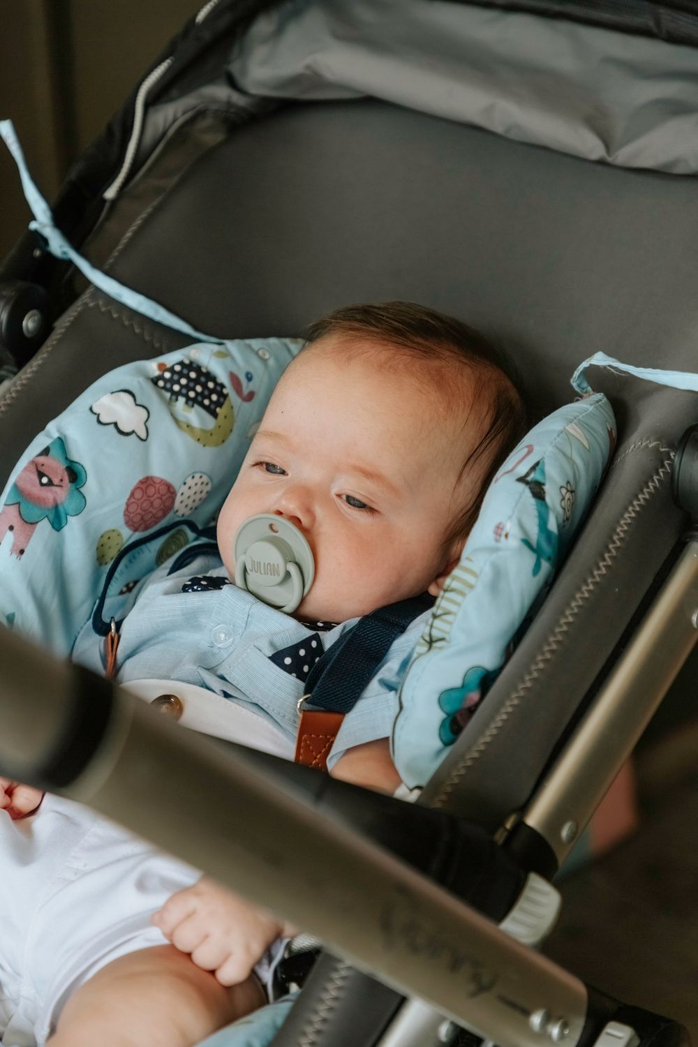 A peaceful baby sleeps in a stroller with blue patterned cushioning.