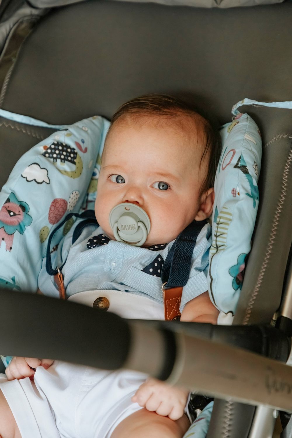 Baby wearing light blue patterned outfit with pacifier rests in stroller.