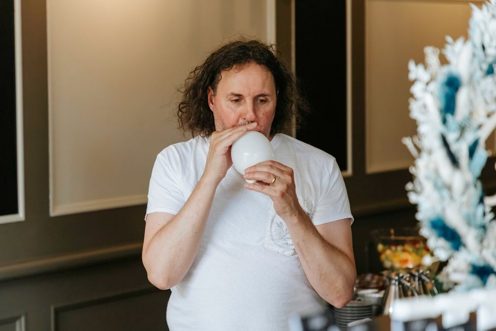 Person in white t-shirt holds and drinks from cup in interior space.