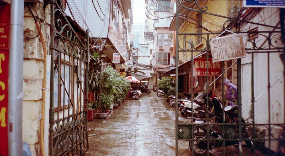 A narrow alleyway in Vietnam with traditional architecture, power lines, and parked motorbikes.