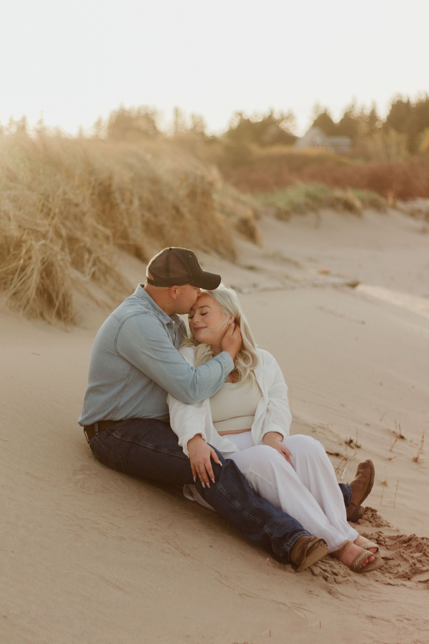 Couple sits close together on beach sand during golden hour.