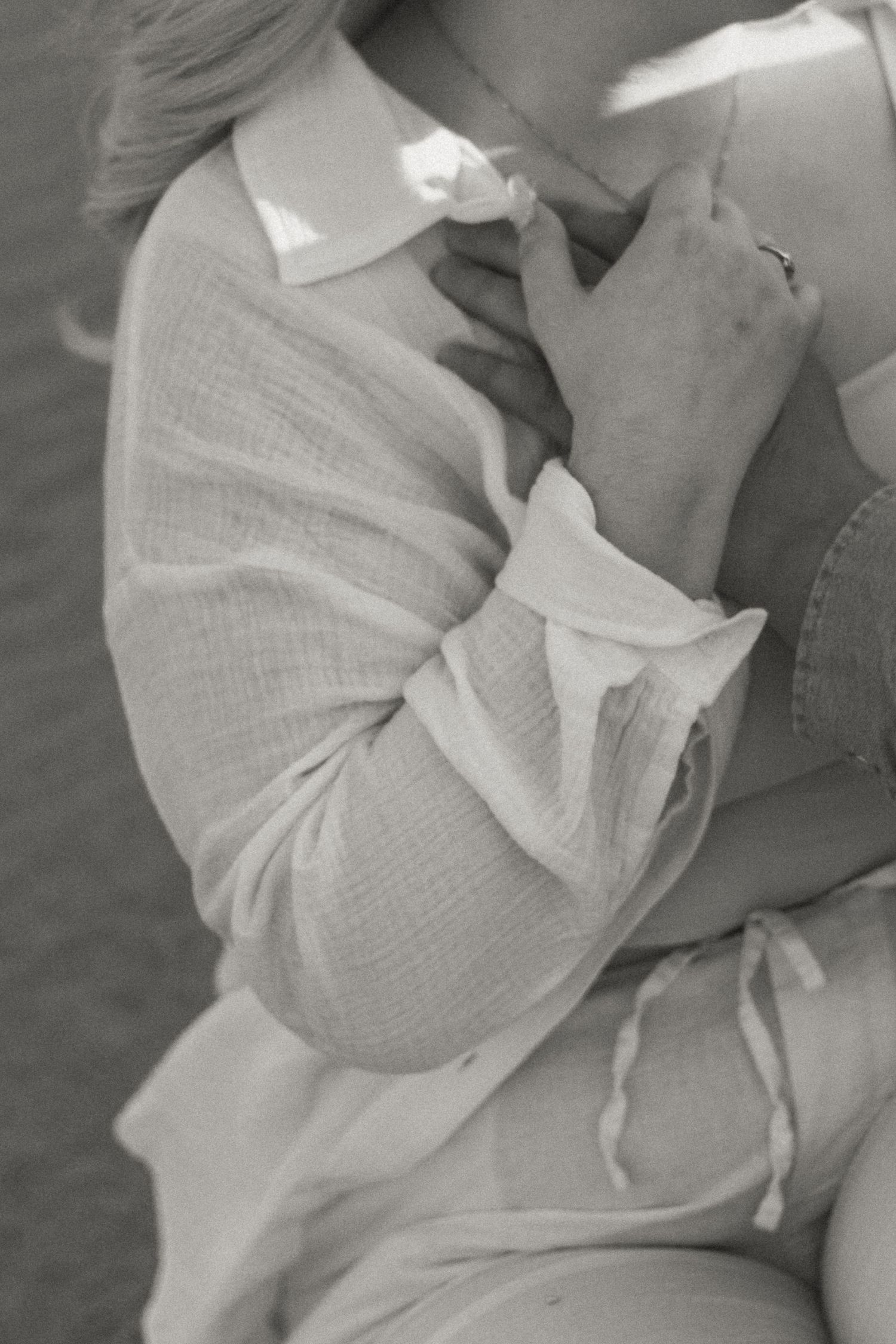A person in a white linen shirt holds their hand near their face in a black and white photograph.