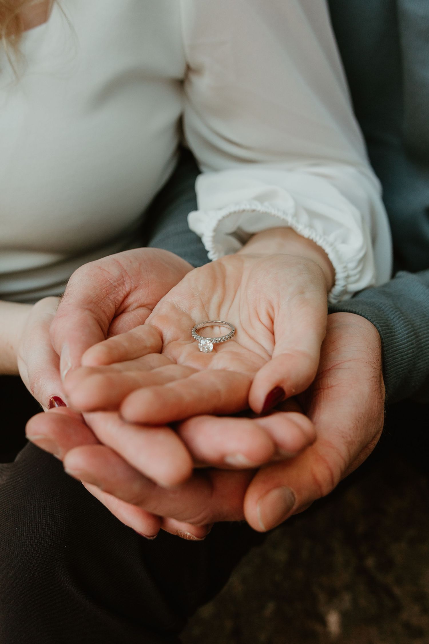 Hands cupped together holding a delicate engagement ring in an intimate moment.