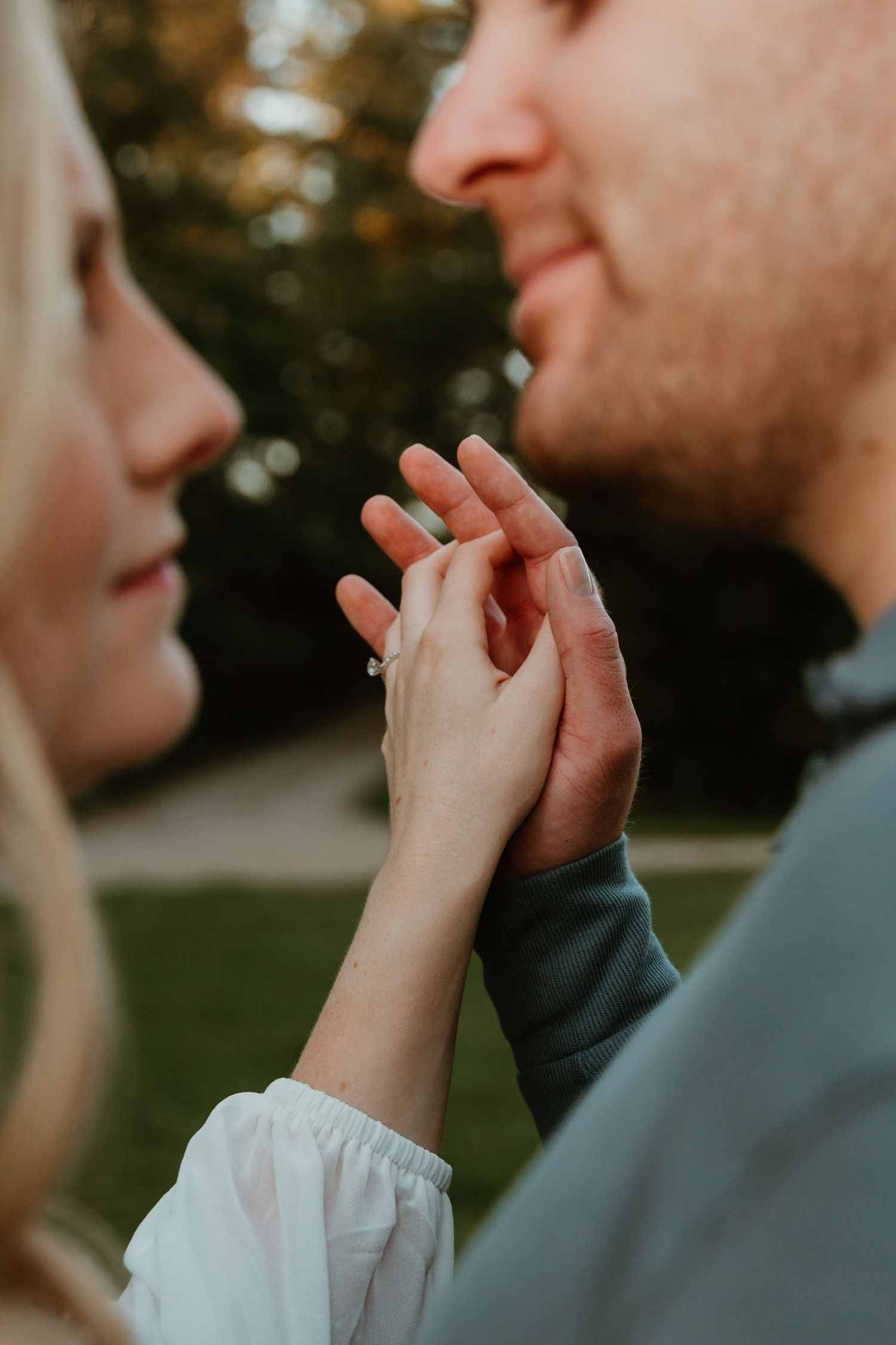 Close-up of hands touching tenderly during an intimate engagement moment outdoors.
