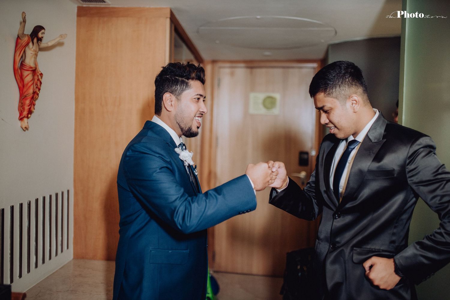 Two people in formal attire playfully interact in a hallway with orange-tinted walls.