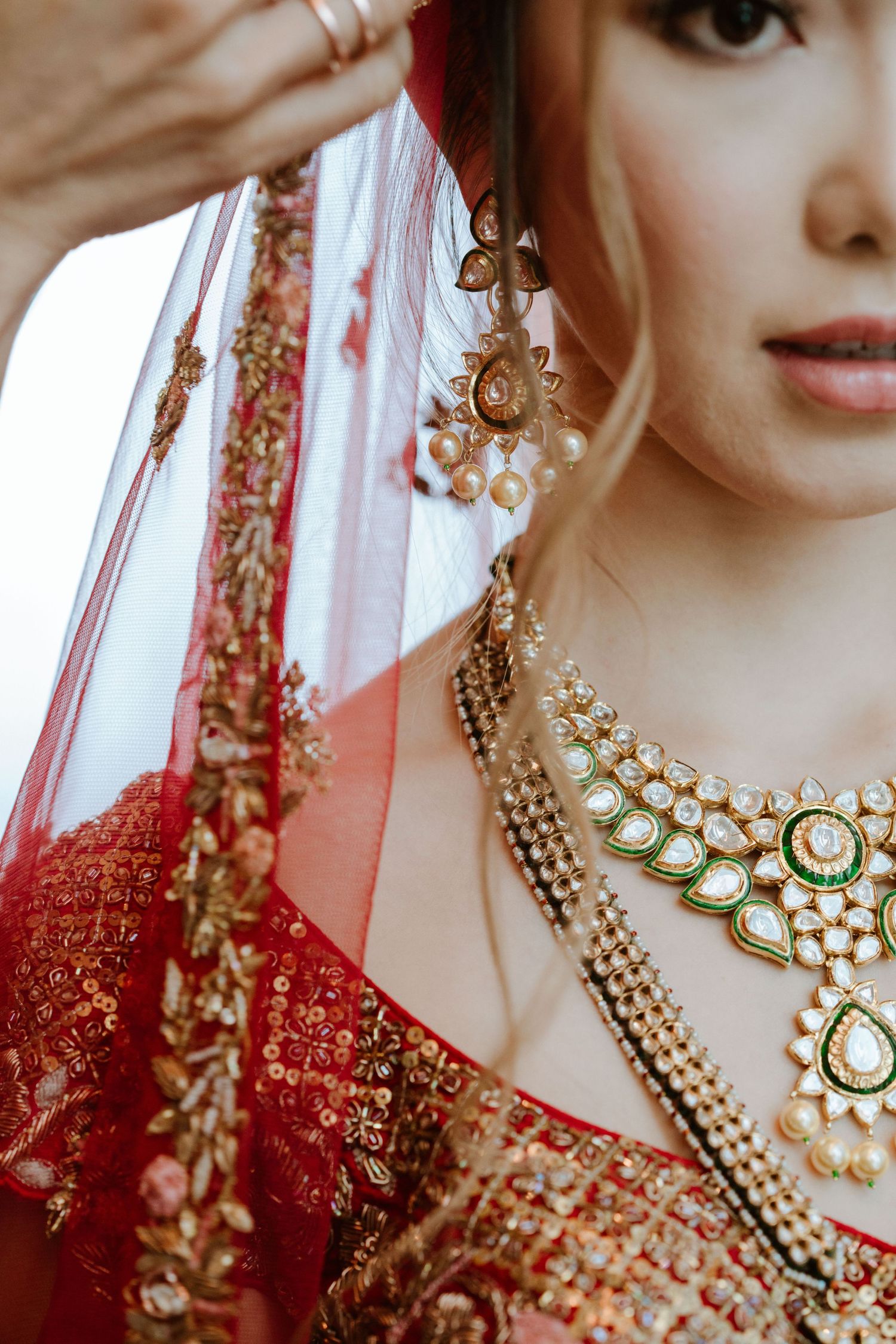 Close-up detail of ornate gold and kundan jewelry with red embroidered fabric from traditional Indian bridal attire.