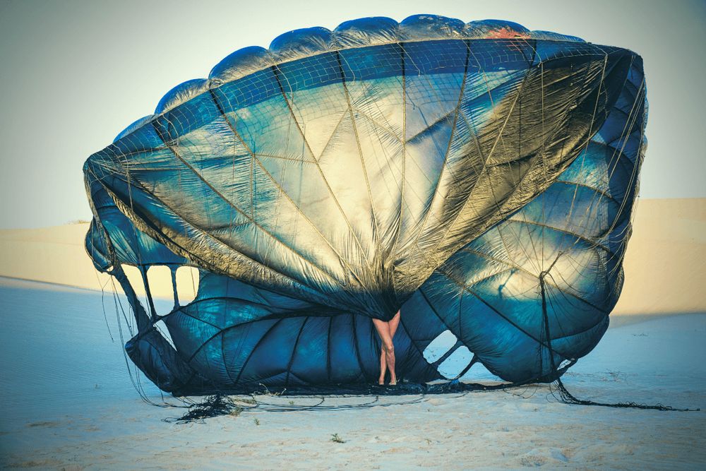 Large blue parachute collapsed on beach at sunset creating dramatic silhouette.