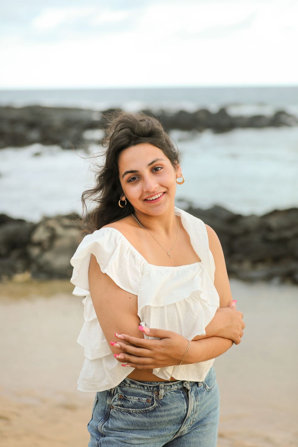 Beachside portrait in white ruffle top and classic denim with natural coastal scenery.