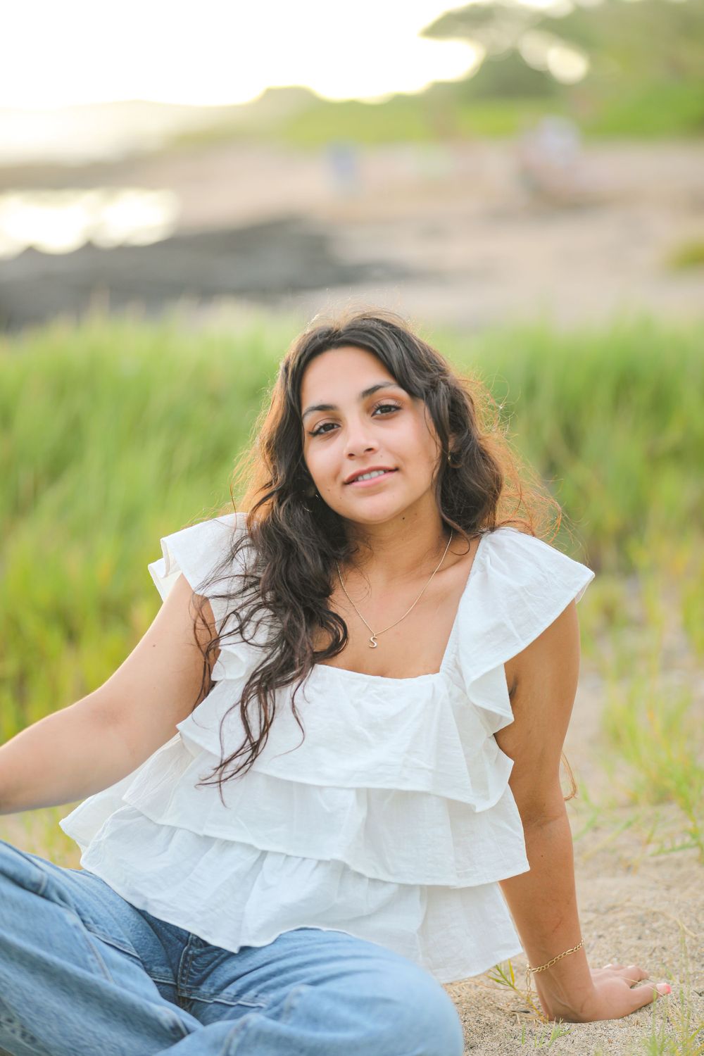 Woman in white ruffled top relaxes on beach path during golden hour.