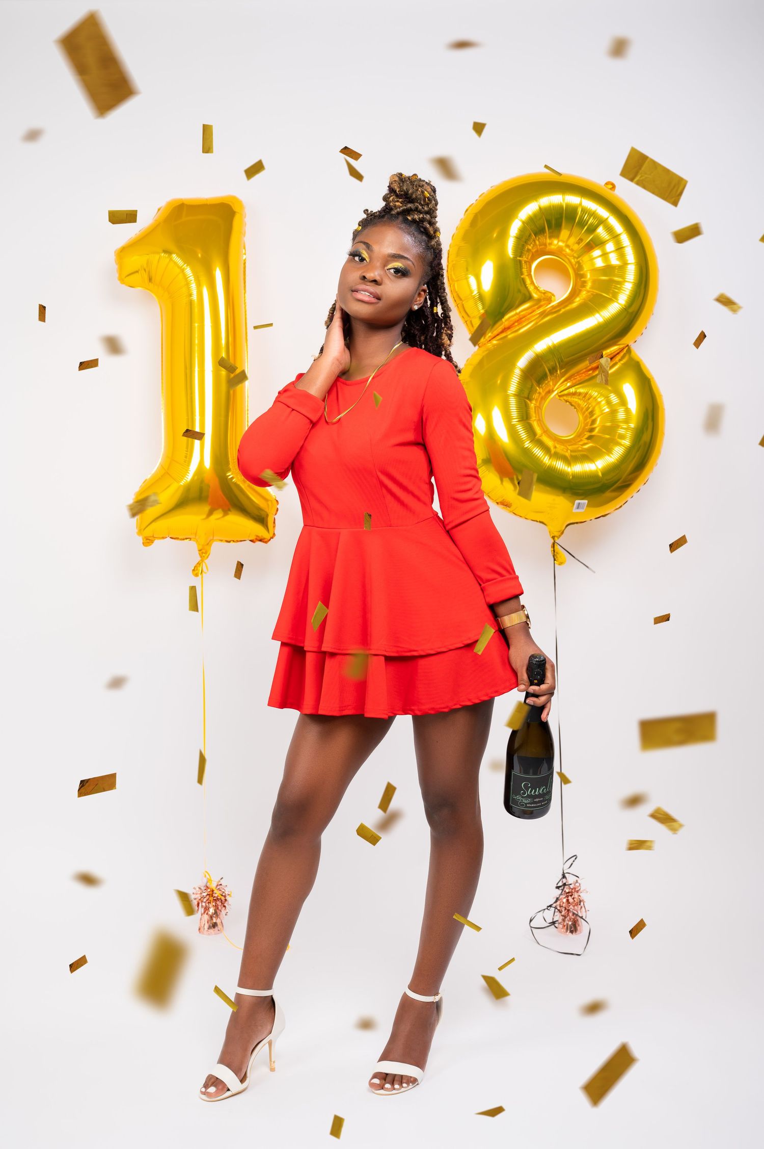 Celebratory photo with large gold number 18 balloons, red dress, and falling gold confetti against white background.