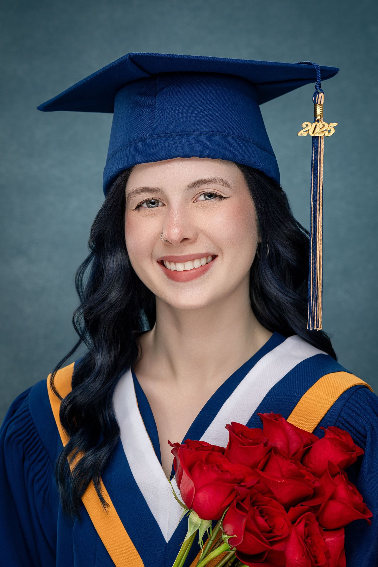 Graduate wearing blue cap and gown holds vibrant red roses during graduation photo session.
