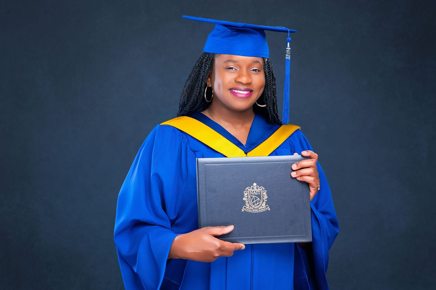 Graduate in blue cap and gown holds diploma while smiling during graduation ceremony celebration.