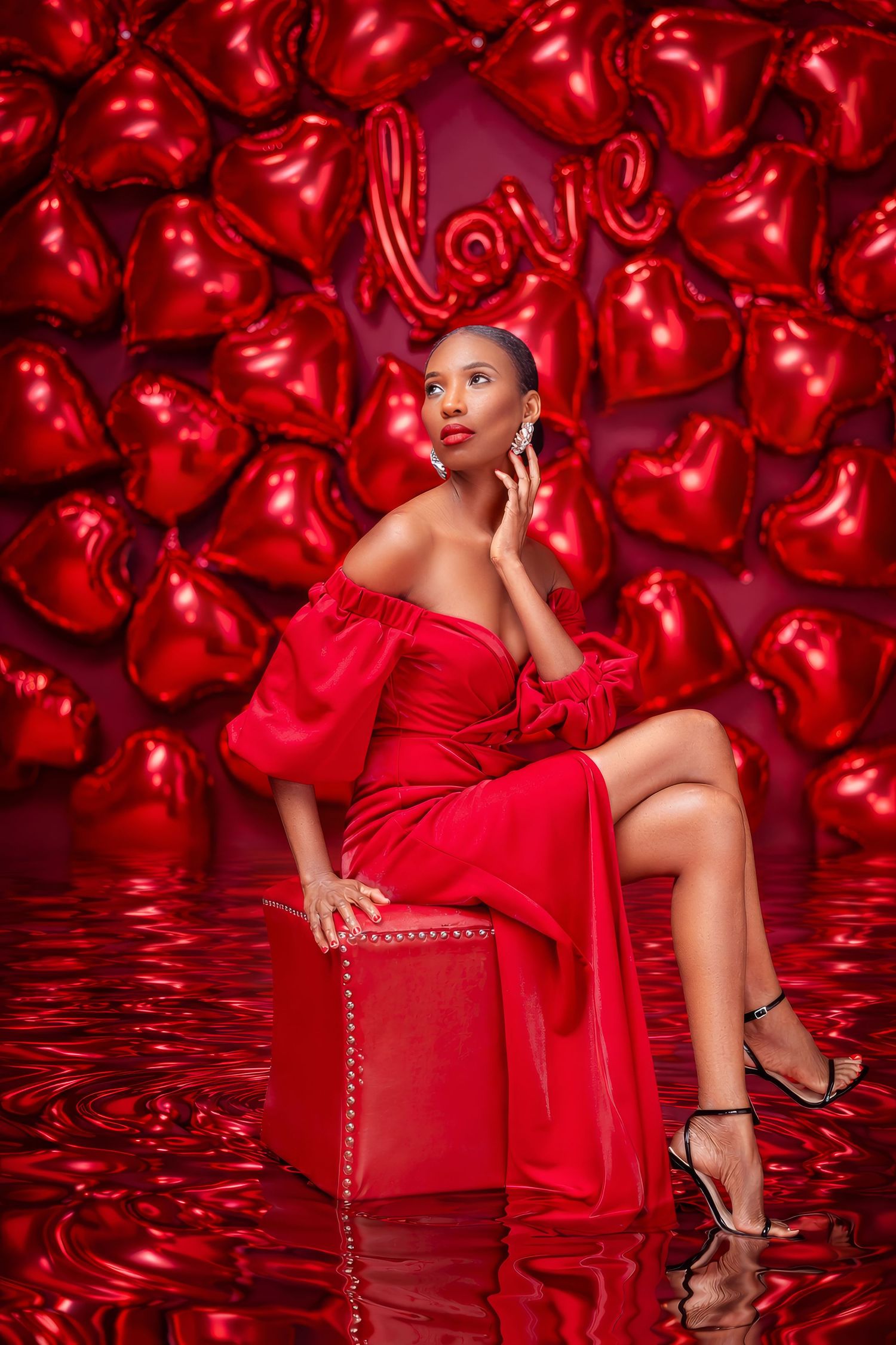 Glamorous fashion photo against red backdrop with metallic heart balloons and reflective floor.