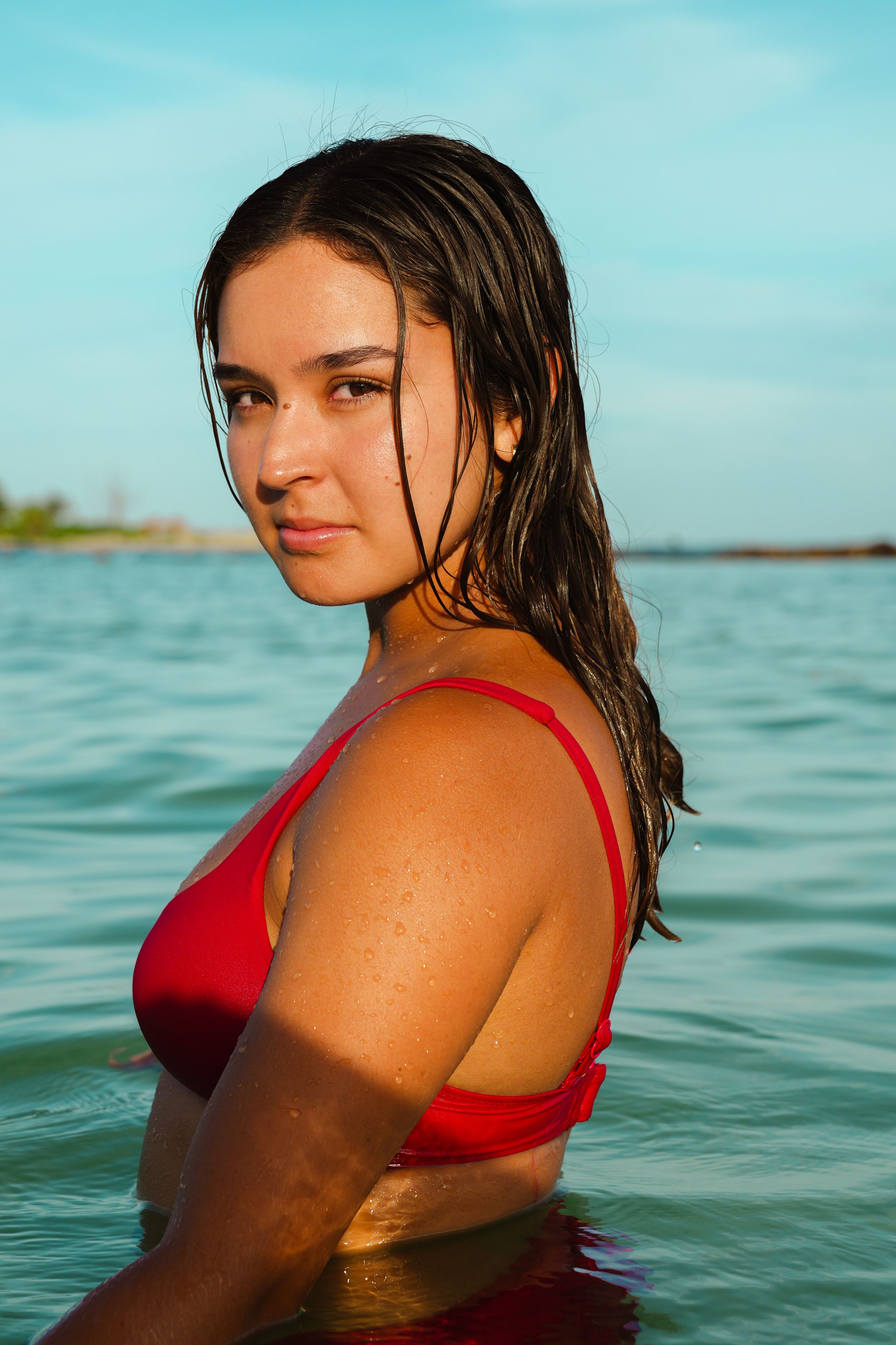 A woman in a red swimsuit poses in turquoise water on a sunny day.