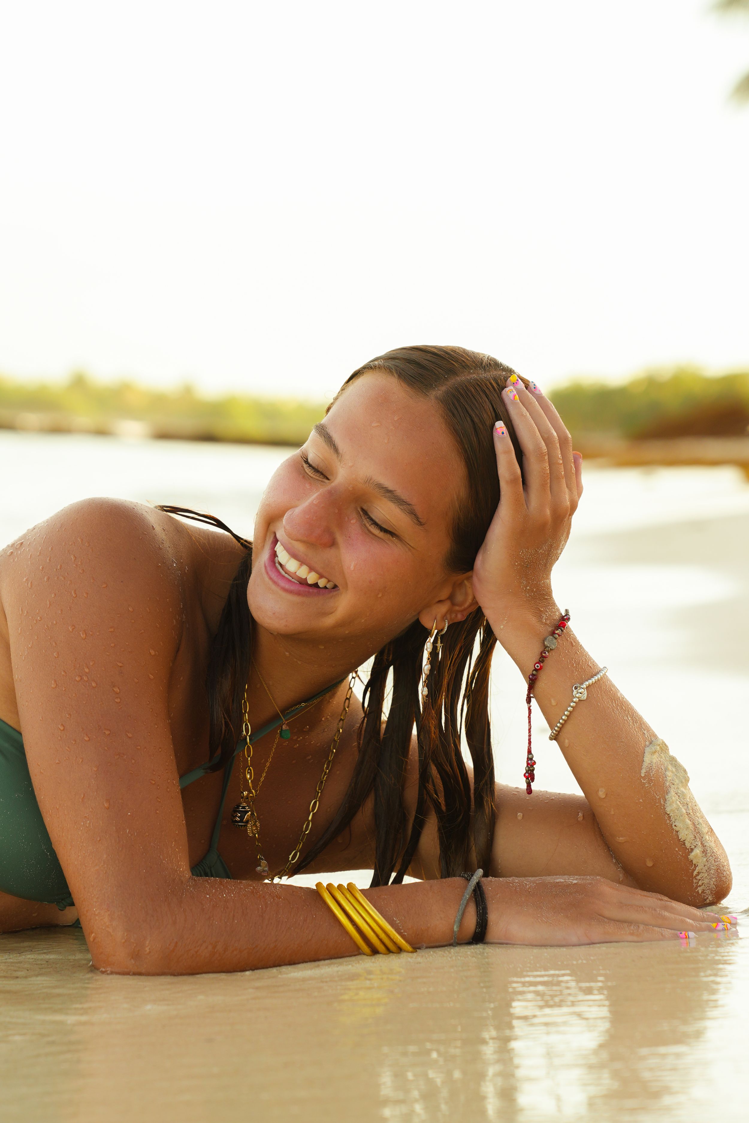 A woman relaxes on a beach at sunset with wet hair and jewelry.