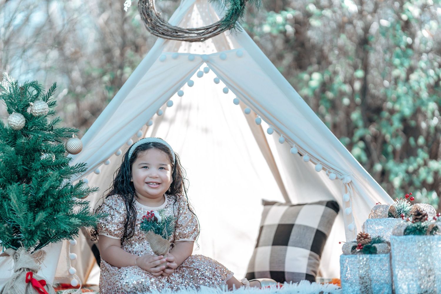 Child sits in front of decorated white teepee tent with holiday decorations.