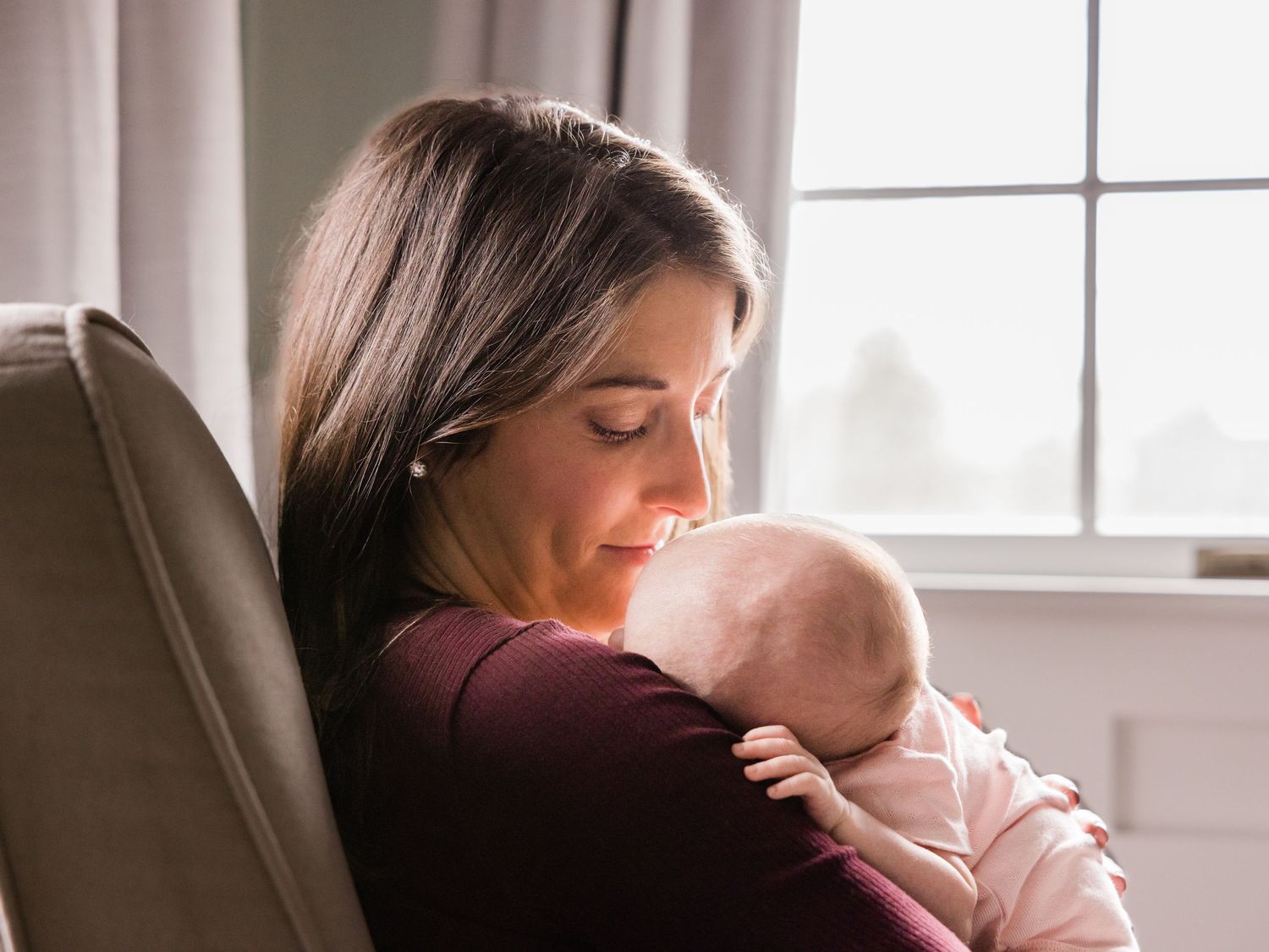 In-home infant lifestyle photo of new mother looking at sleeping baby in arms