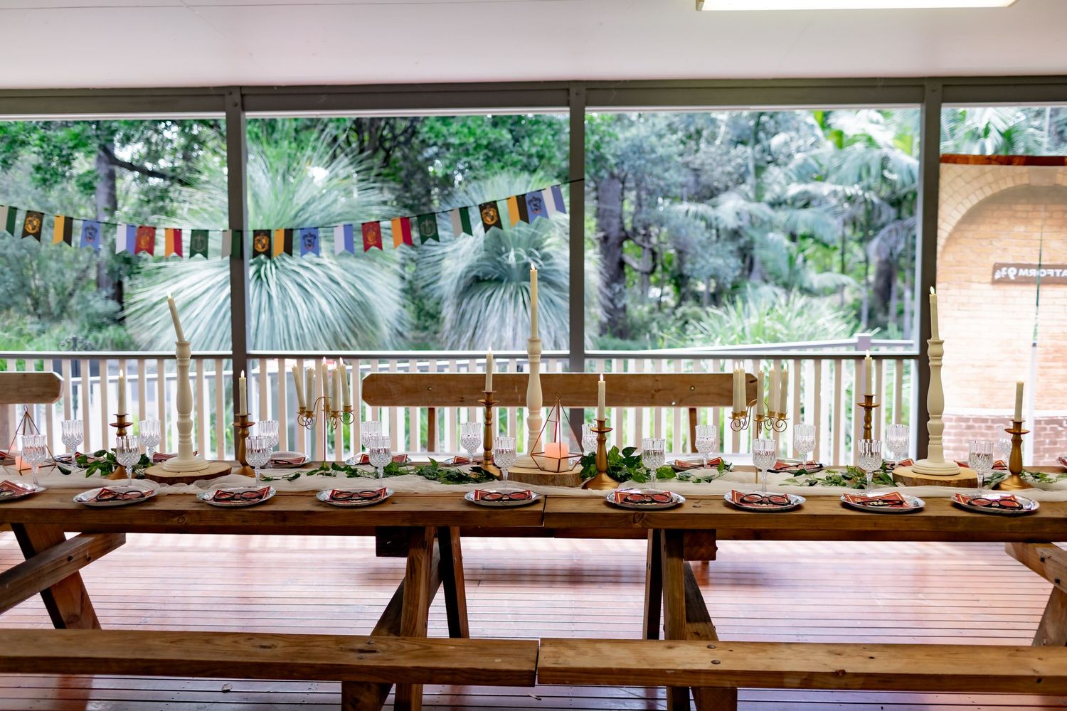 Rustic outdoor reception setup with colorful bunting and picnic-style wooden tables on a covered porch.
