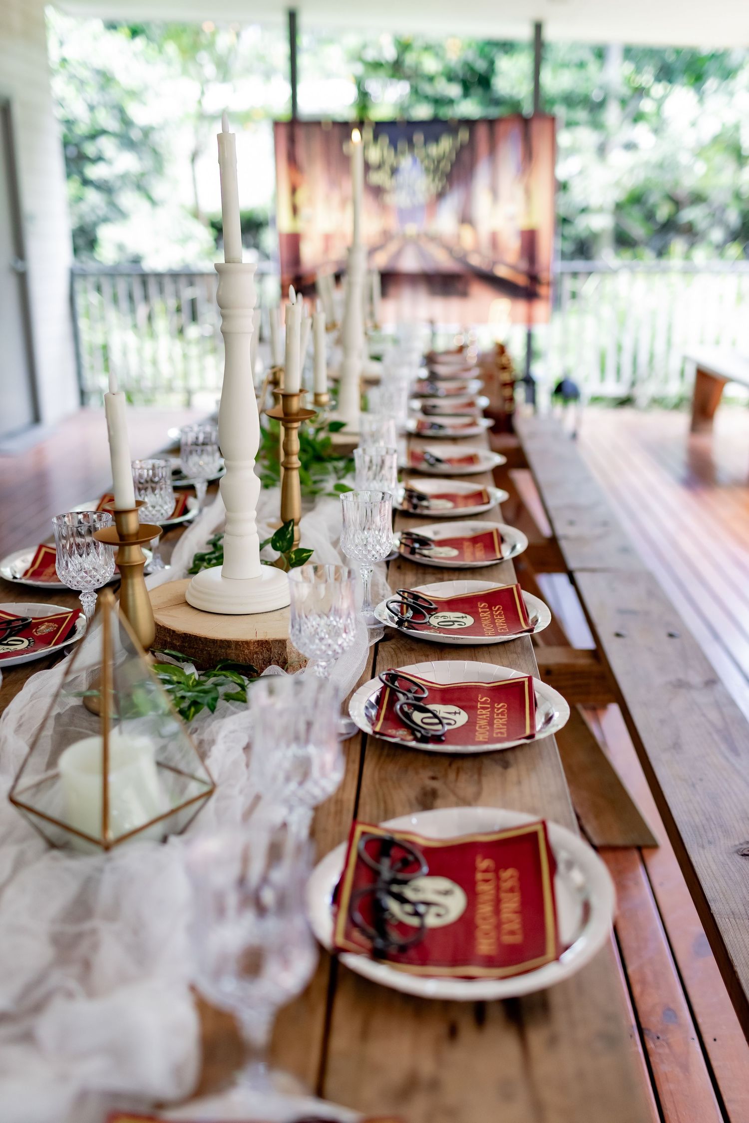 Beautifully set rustic table with white candles, geometric centerpieces, and red place settings on a wooden deck.