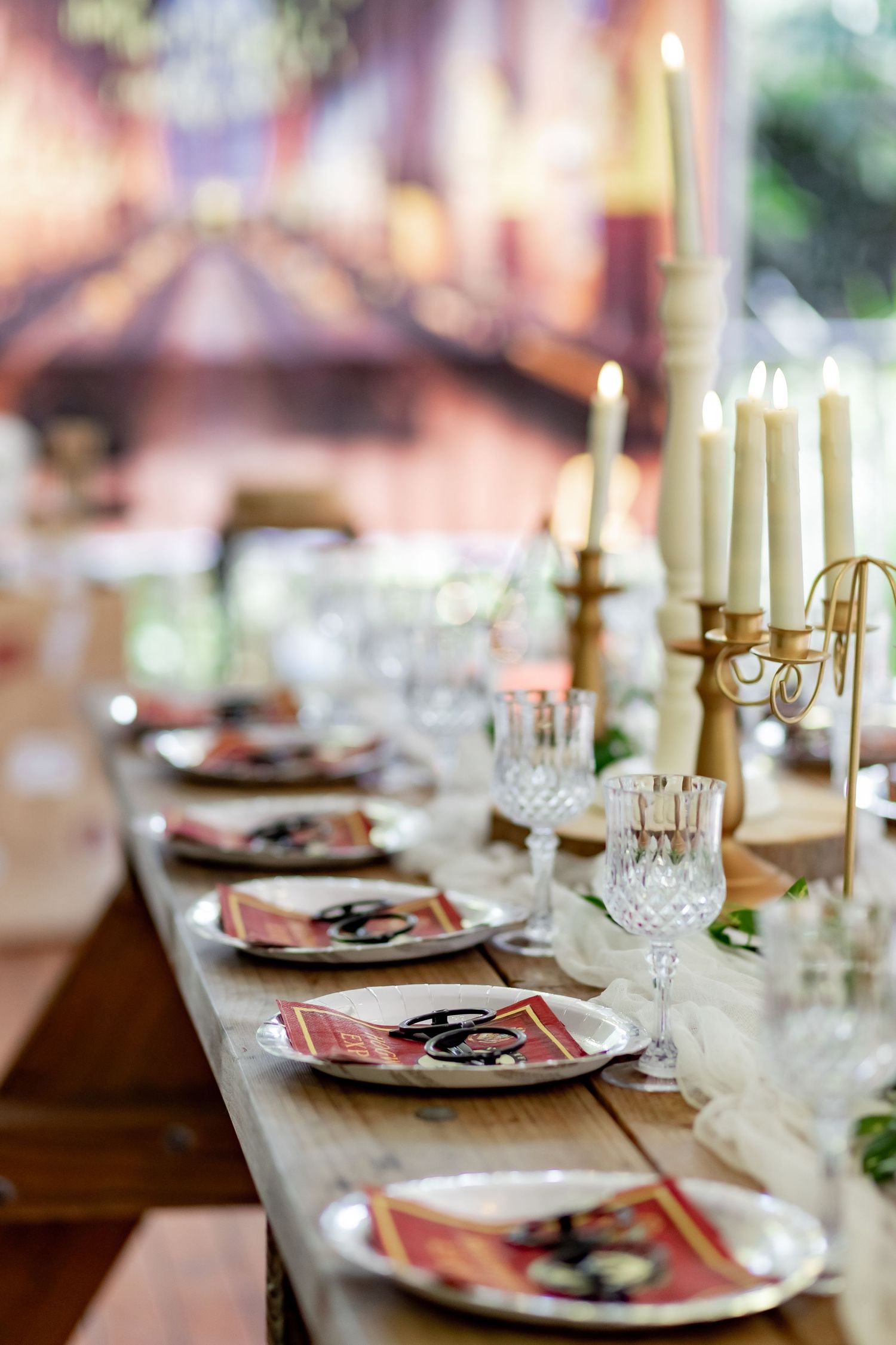 Elegant table setting with tall white candles, crystal glasses, and themed place settings in warm lighting.