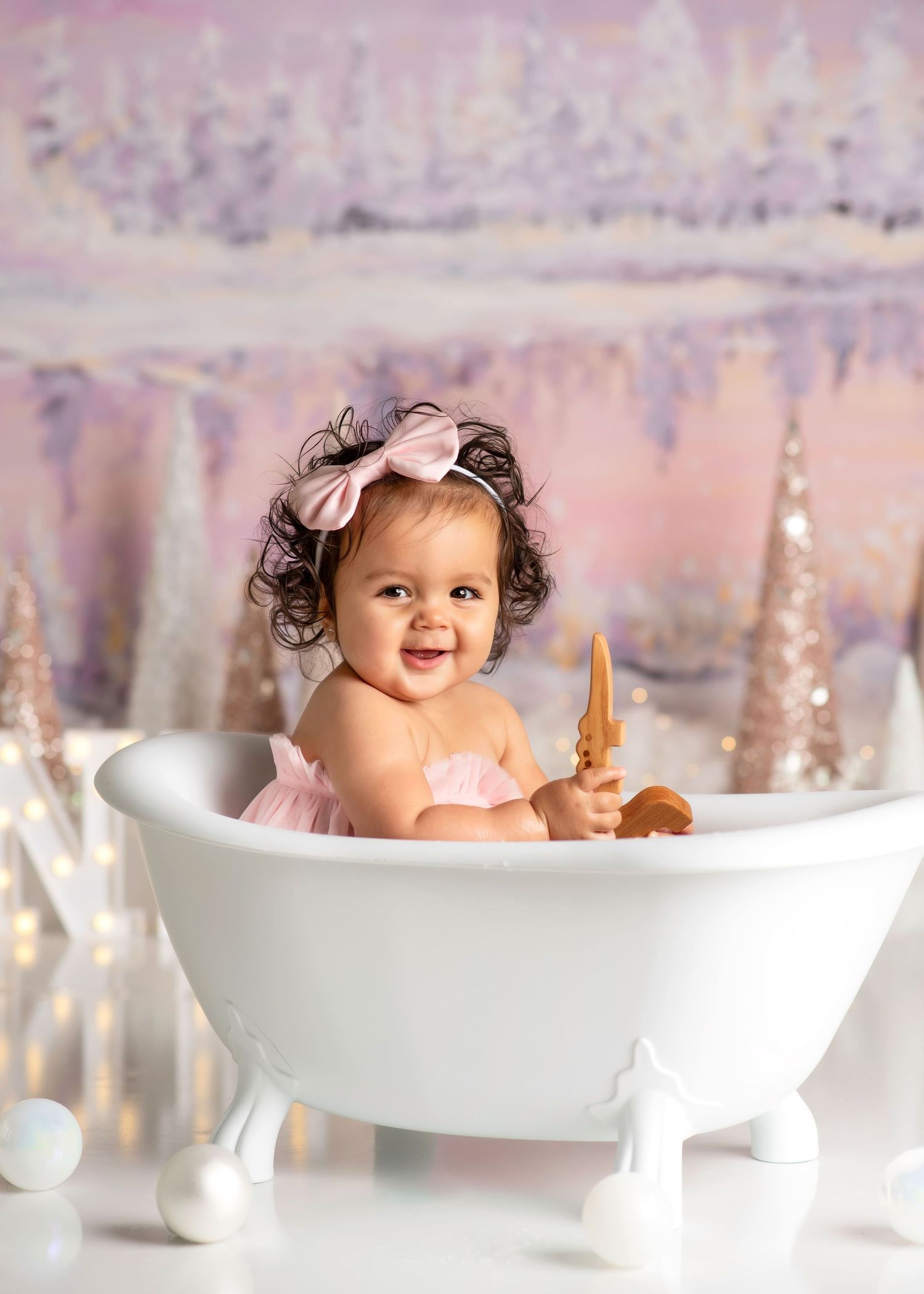 a baby smiles from a tiny bathtub while holding a wooden toy