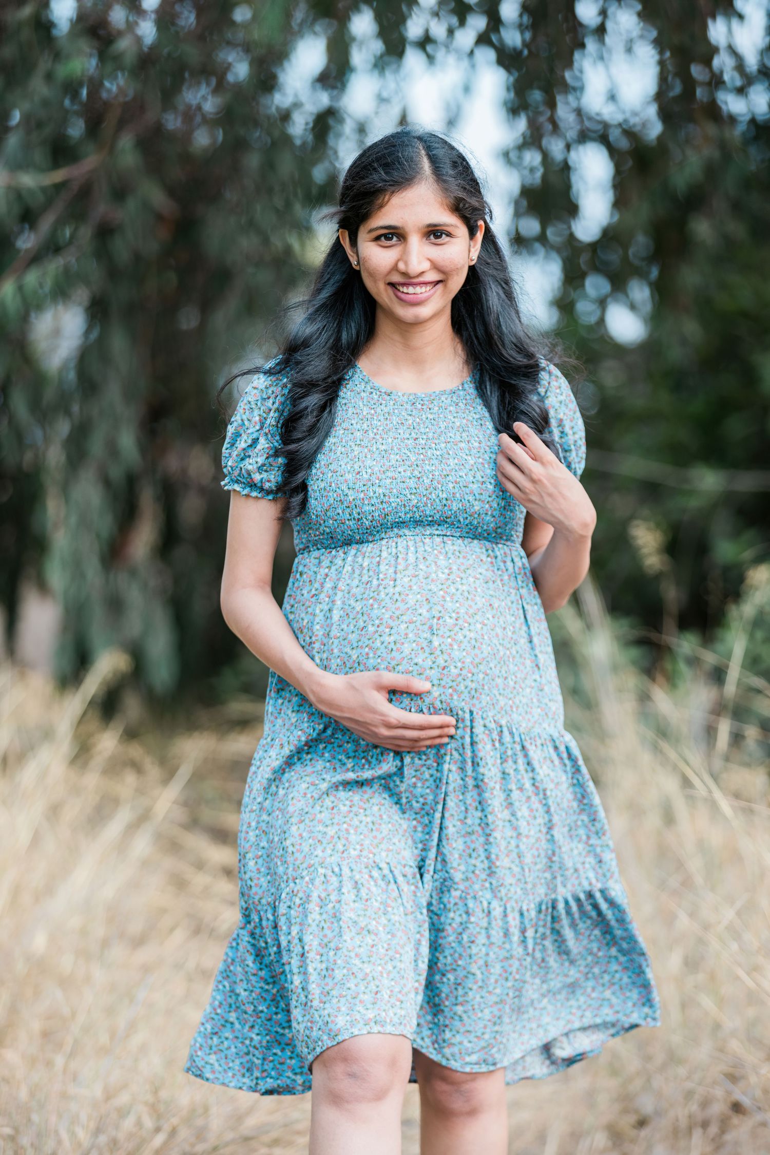 Maternity portrait in a blue floral dress against a natural outdoor setting.