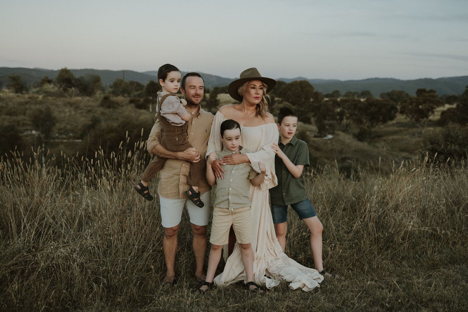 A family group poses together on a hilltop during sunset wearing casual attire.