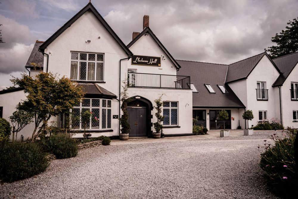 White exterior of The Coach House venue with gravel driveway and manicured landscaping under moody skies.