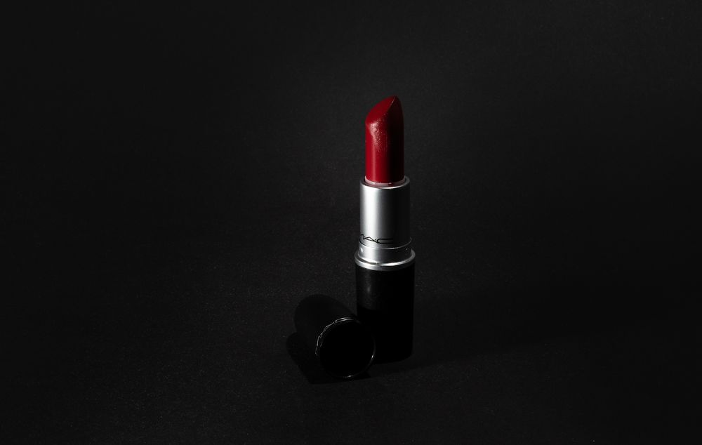 A classic red lipstick in silver tube photographed dramatically against black background.