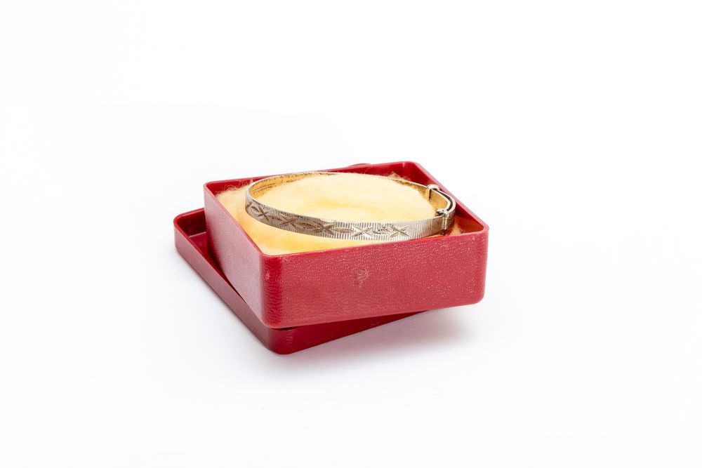 Red square vintage jewelry box containing gold bracelet.