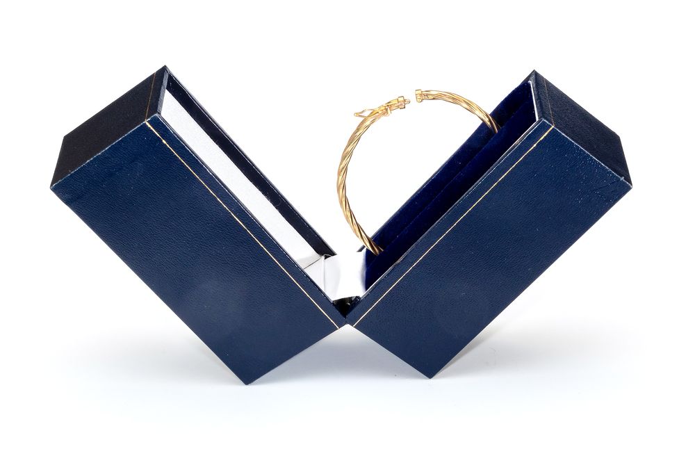 Gold bracelet displayed between two navy blue jewelry boxes.