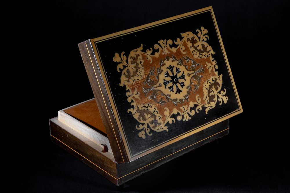 An ornate vintage wooden box with intricate gold floral designs on dark background.