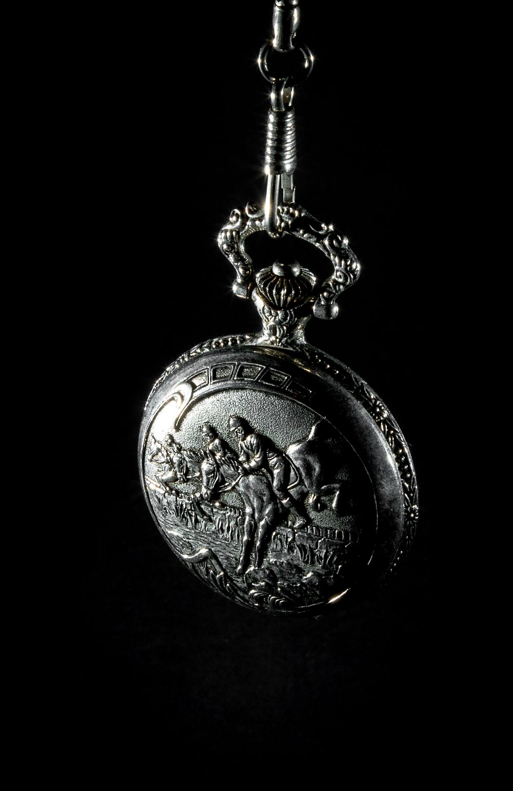 A vintage silver pocket watch with decorative engraving photographed dramatically on black.