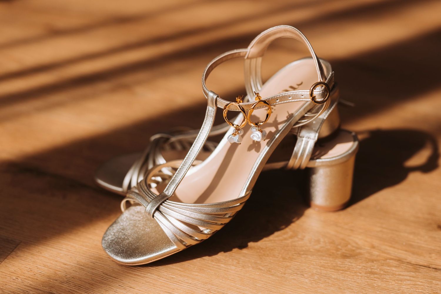 Metallic silver wedding shoes with t-strap design on wooden surface in sunlight.
