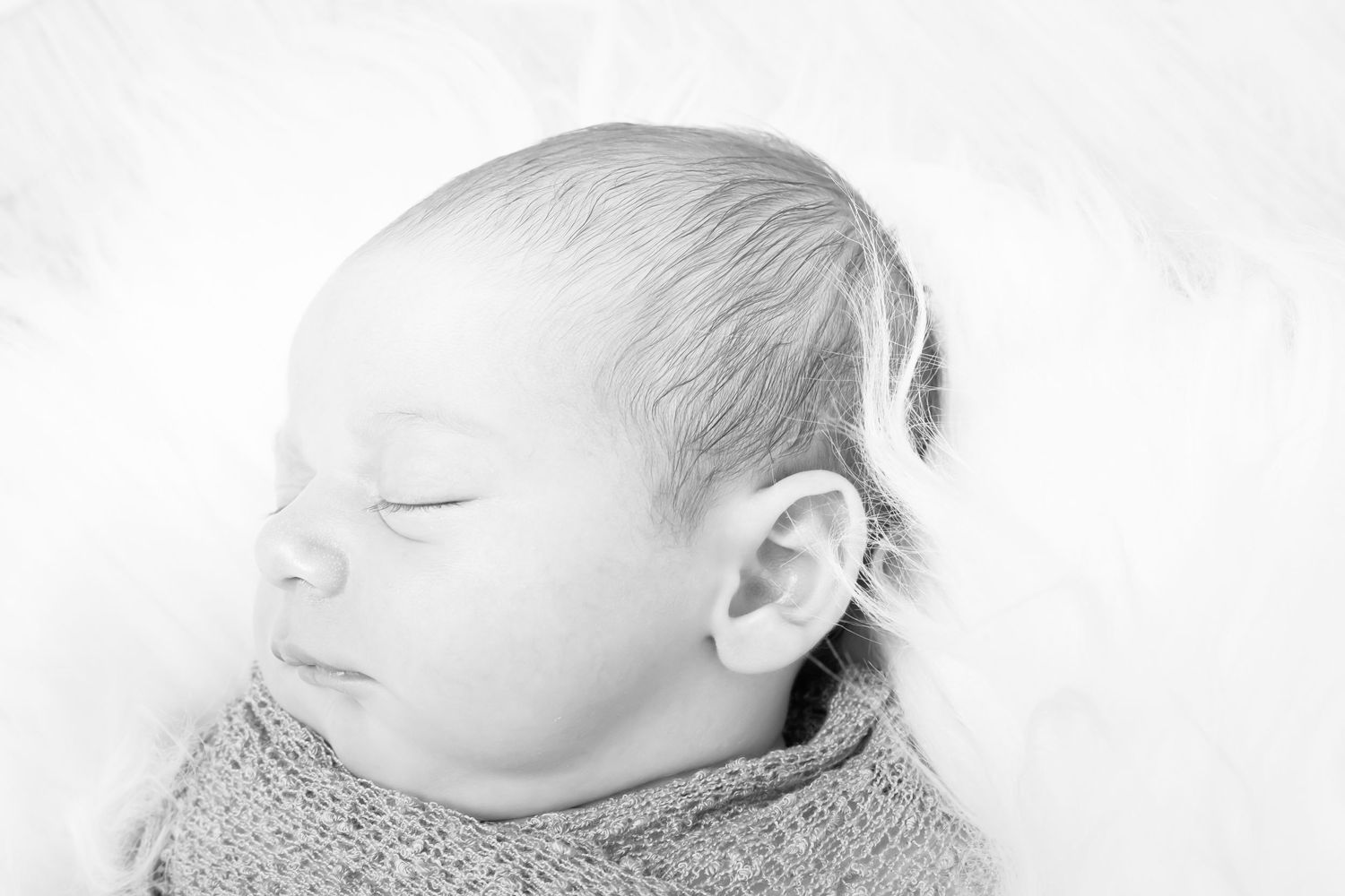 Serene black and white portrait of a peaceful sleeping newborn wrapped in soft fabric.