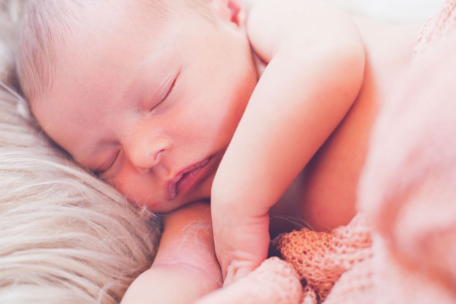 Close up of sleeping infant wrapped in pink blanket on furry backdrop.