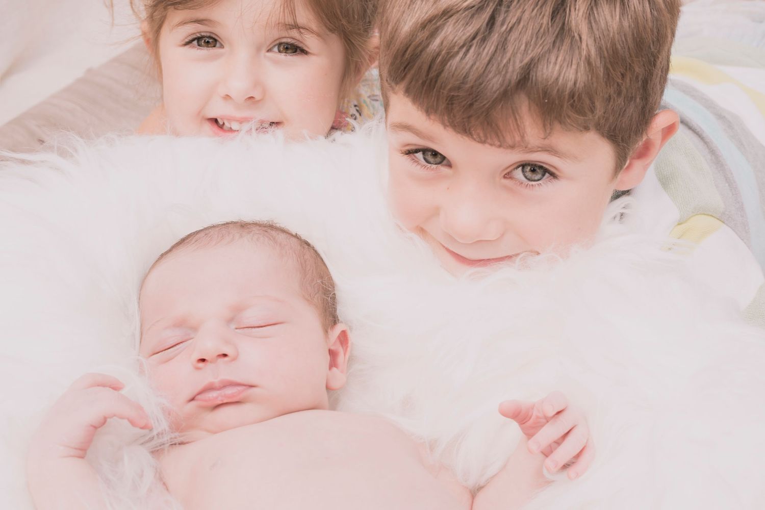 Tender moment showing three siblings together on white bedding.