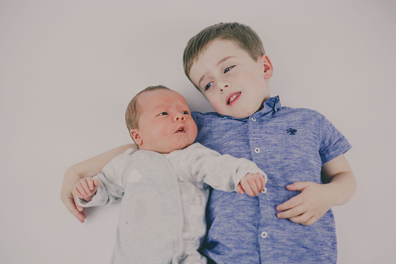 Two children lying together and sharing tender moment on light background.