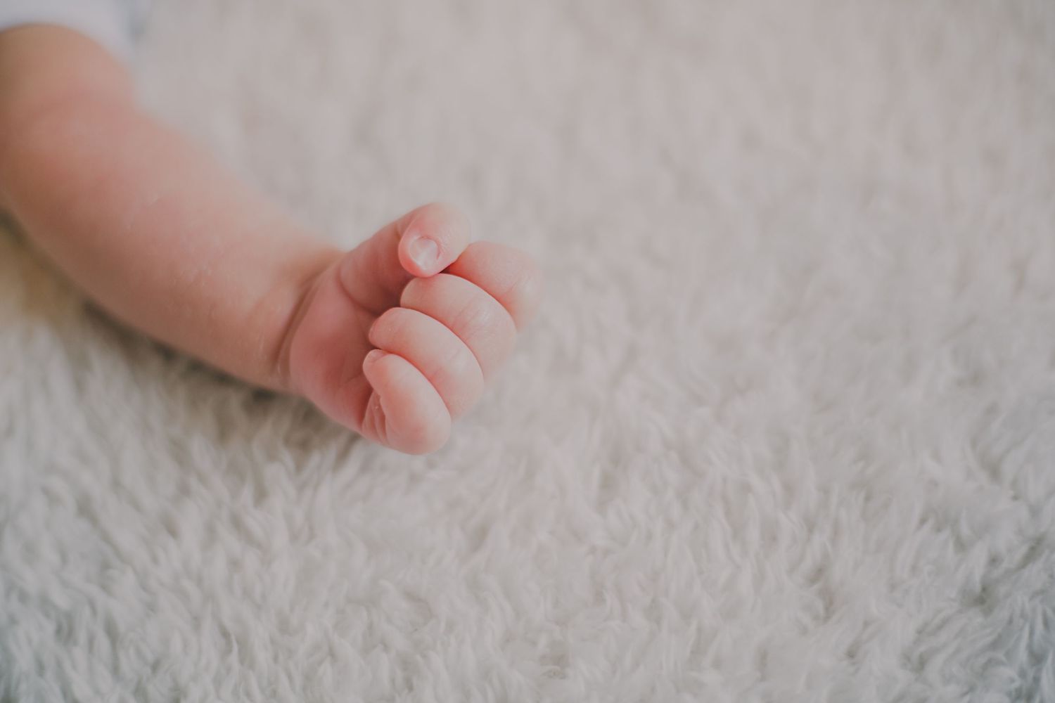 Close-up of tiny baby hand against white fluffy carpet texture.