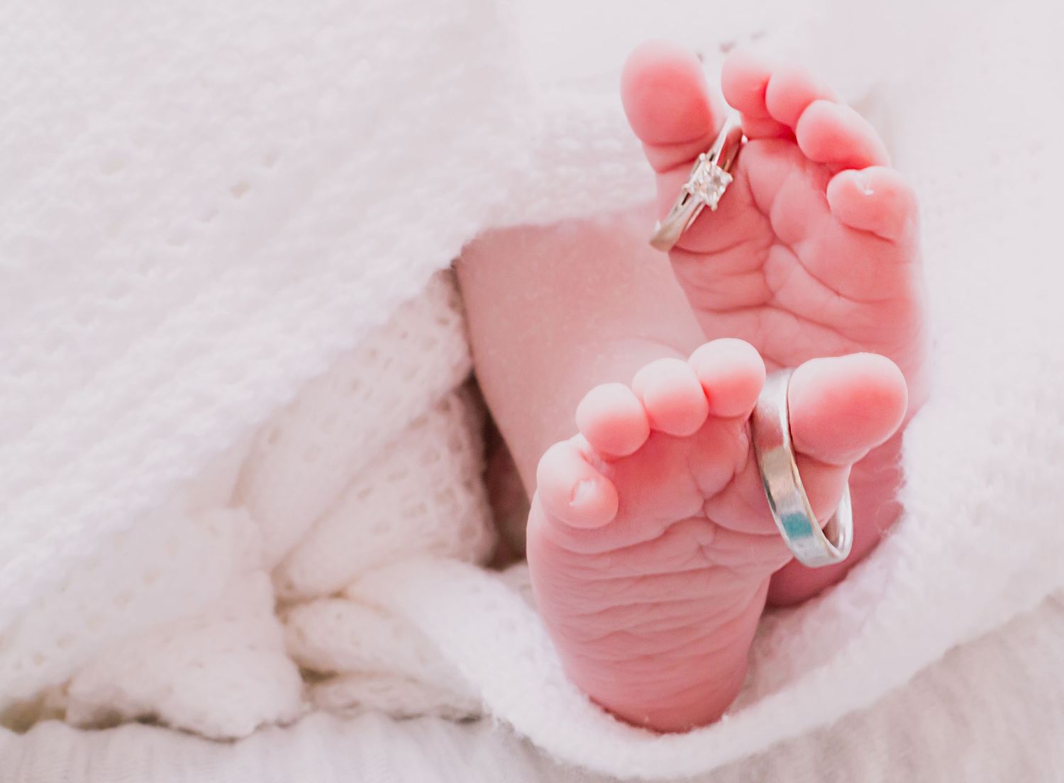 Close-up of tiny newborn feet with decorative pins against white fabric.