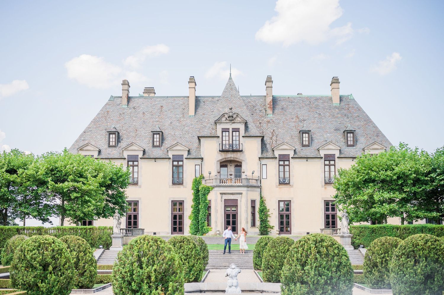 Couple holding hands and gazing at each other in front of the majestic Oheka Castle.