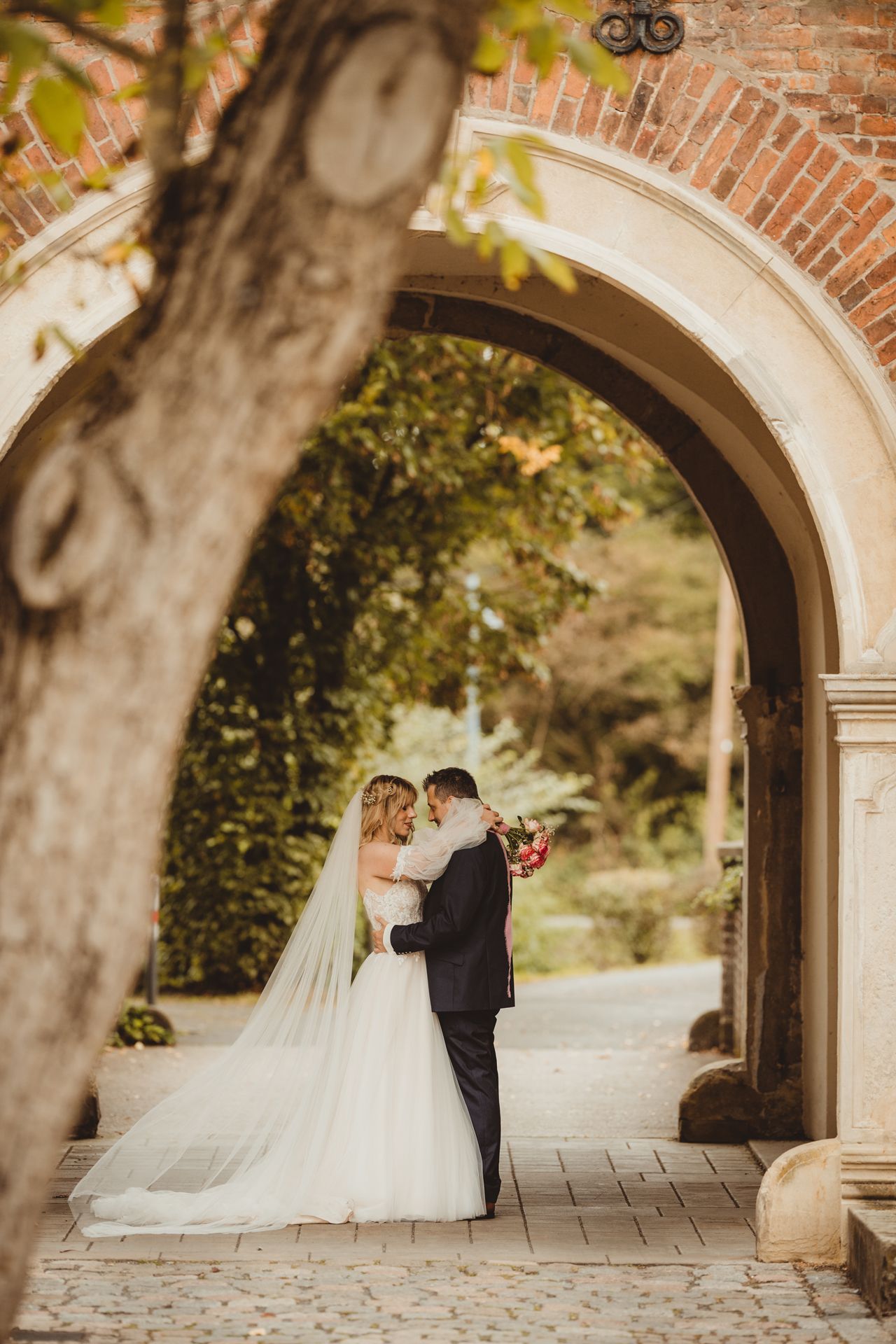 Newlyweds share an intimate moment under a beautiful brick archway in a garden setting.