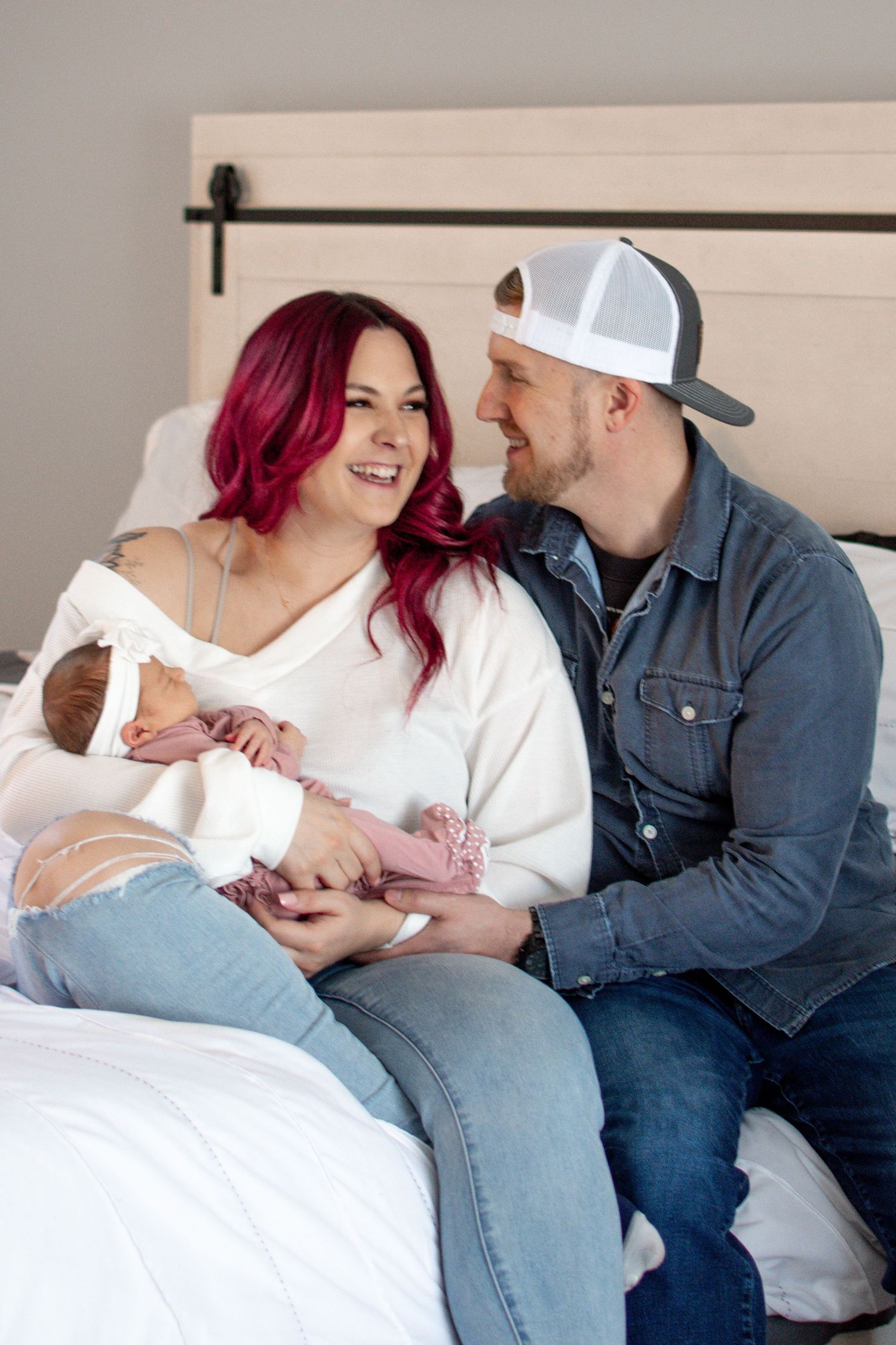 Couple sitting on bed with newborn baby in casual attire.