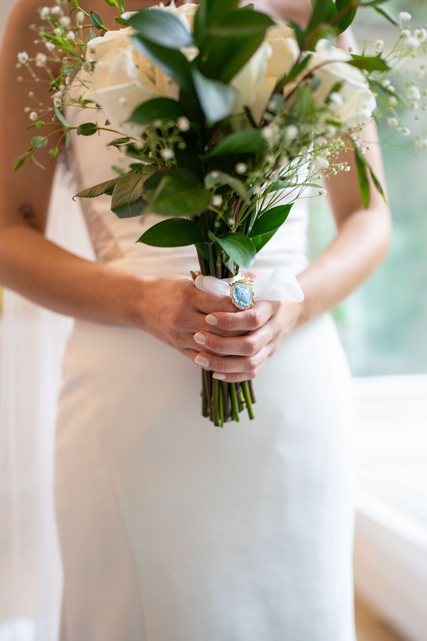 A classic white and green wedding bouquet with roses and foliage held by someone in a white dress.