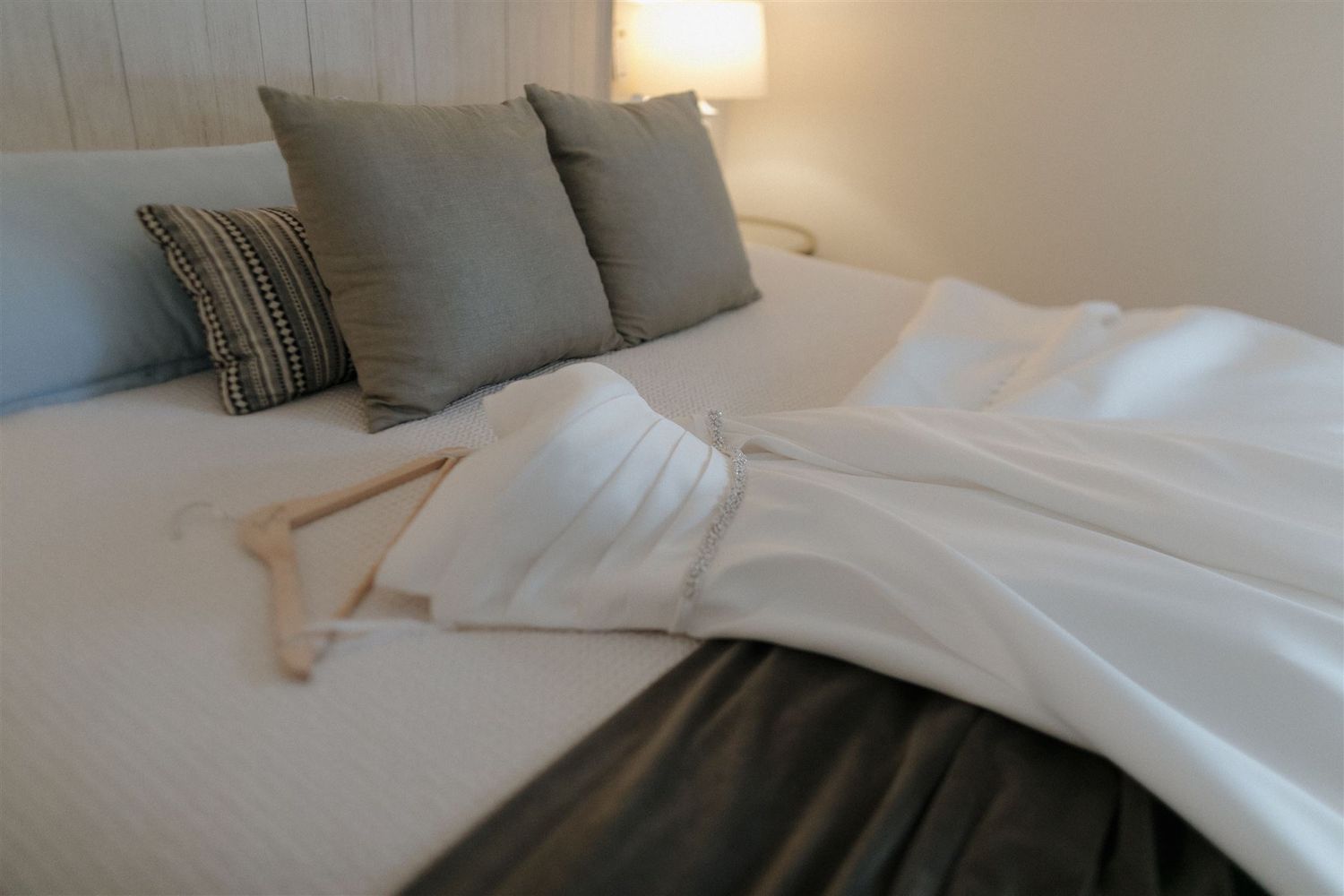 A neatly made bed with white linens and grey pillows in a bright bedroom.