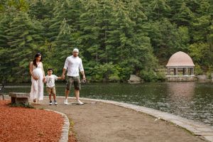A family walks together on a lakeside path near a gazebo.